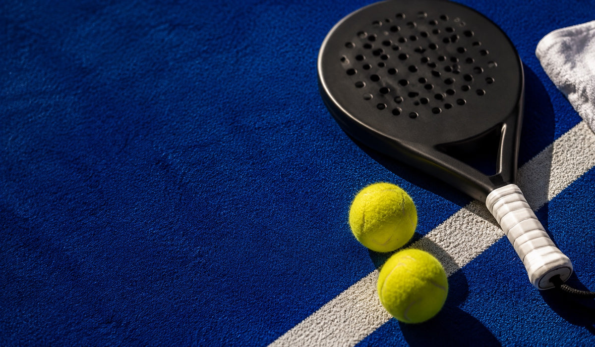 Padelracket en twee ballen op een blauwe padelbaan